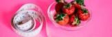 A glass bowl of fresh strawberries paired with a pink measuring tape symbolizes healthy eating.